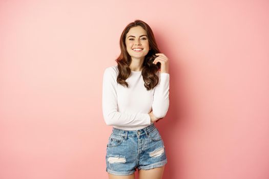 Spring and beauty. Young beautiful and stylish female model posing against pink background, cross arms on chest, smiling happy.