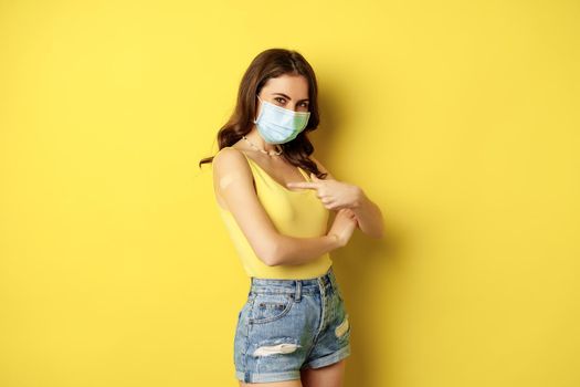 Covid-19 vaccination. Beautiful young woman in face medical mask got vaccinated during pandemic, standing over yellow background.