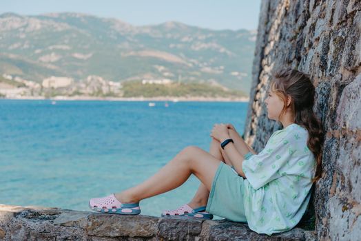 Beautiful girl sitting on a stone wall, in background is the blue sea, Budva, Montenegro