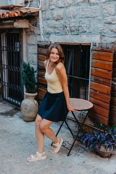 Girl tourist walking through ancient narrow street on a beautiful summer day in MEDITERRANEAN MEDIEVAL CITY , OLD TOWN bUDVA, MONTENEGRO. Young beautiful cheerful woman walking on old street at tropical town. Pretty girl looking at you and smiling