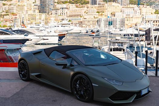 Luxury sport car of dark color is in port Hercules of Monaco in shadow, Monte-Carlo, very aggressive view of roadster, cabriolet, a lot of boats and yachts are on background. High quality photo