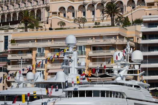 A lot of huge yachts are in port of Monaco at sunny day, Monte Carlo, real estate housing is on background, glossy board of the motor boat, megayachts are moored in marin. High quality photo