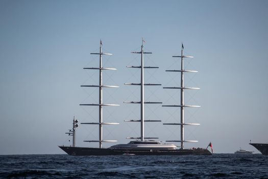 A huge sail yacht of conceptual design with three masts stands in the bay near Monaco at sunny day, the sails are lowered, the yacht spins around its anchor, left side of the sailboat, clear weather. High quality photo