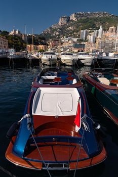A lot of motor boats in rows are in port of Monaco at sunny day, Monte Carlo, mountain is on background, colourful interior of the boat, are moored in marina, sun reflection on glossy board. High quality photo