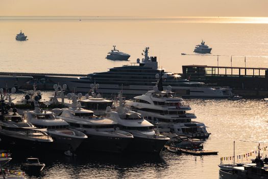 A lot of huge yachts are in port of Monaco at sunrise, glossy board of the motor boat, the chrome plated handrail, megayachts are moored in marina, sun reflections, water surface on background. High quality photo