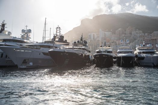 A lot of huge yachts in port of Monaco at sunset, mountain is on background, glossy board of the motor boat, megayachts are moored in marina, sun reflection on glossy board, backlight. High quality photo