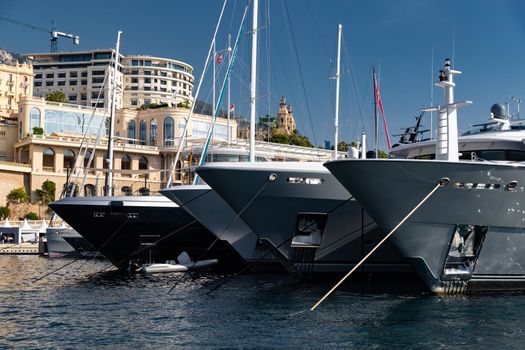 A lot of huge yachts are in port of Monaco at sunny day, Monte Carlo, mountain is on background, glossy board of the motor boat, megayachts are moored in marina, sun reflection on glossy board. High quality photo