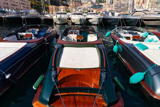 A lot of motor boats in rows are in port of Monaco at sunny day, Monte Carlo, mountain is on background, colourful interior of the boat, are moored in marina, sun reflection on glossy board. High quality photo