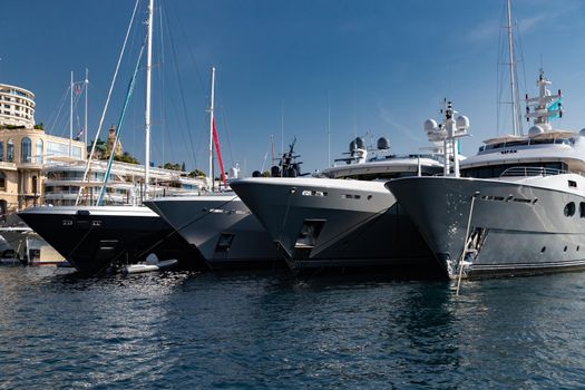 A lot of huge yachts are in port of Monaco at sunny day, Monte Carlo, mountain is on background, glossy board of the motor boat, megayachts are moored in marina, sun reflection on glossy board. High quality photo