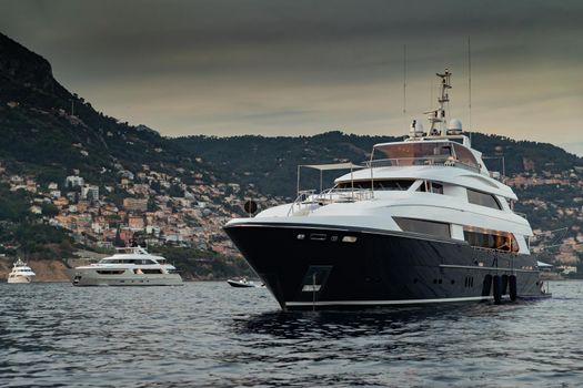 The huge yacht in sea at sunset, glossy dark board of the motor boat, the chrome plated handrail, moored mega yacht, dusk. High quality photo