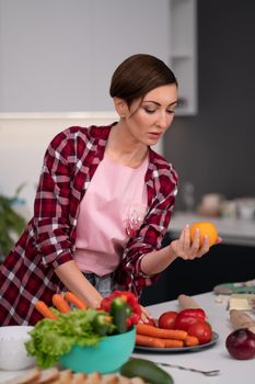 Young pretty housewife with a bob hairstyle prepares food in the kitchen choosing tomato red or yellow. Healthy food at home. Healthy food leaving - vegan concept.