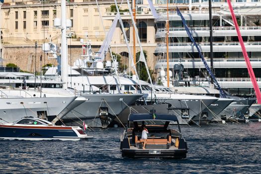 A large boat enters the port, the girl on the deck is talking on the phone, A lot of huge yachts are in port of Monaco on background, Monte Carlo, megayachts are moored in marina, sun reflection. High quality photo
