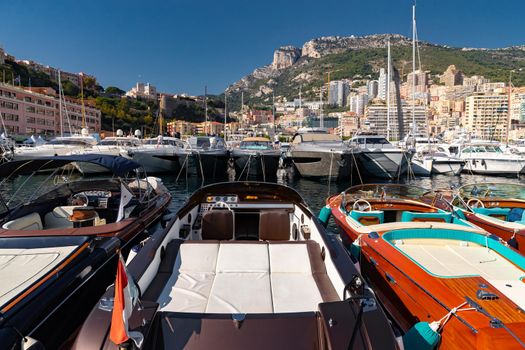 A lot of motor boats in rows are in port of Monaco at sunny day, Monte Carlo, mountain is on background, colourful interior of the boat, are moored in marina, sun reflection on glossy board. High quality photo