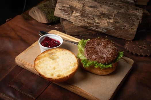 Fresh craft beef burger with cherry sauce in a sauce bowl, fresh lettuce with lead bun laying next with wooden lodges as decoration. Restaurant concept. Street food concept.