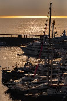 A lot of huge yachts are in port of Monaco at sunrise, glossy board of the motor boat, the chrome plated handrail, megayachts are moored in marina, sun reflections, water surface on background. High quality photo