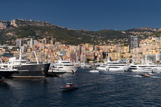 A lot of huge yachts are in port of Monaco at sunny day, megayachts are moored in marina, is a yacht show, Monte Carlo, real estate housing is on background, glossy board of the motor boat. High quality photo