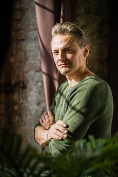 Half-turn Handsome Man of 40s is Standing at the Window With Folded Arms in His Mansion House. Slender Guy in His Antique Castle. Close-up. Portrait. Vintage Background. High quality photo