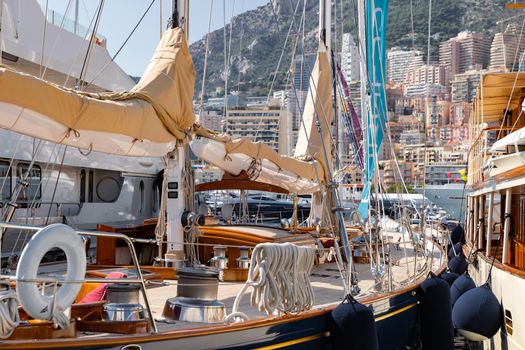 A main deck of sail yacht in classic style, lot of huge yachts are in port of Monaco at sunny day, Monte Carlo, mountains and housing massif are on background, megayachts are moored in marina. High quality photo