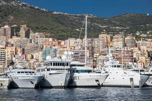 A lot of huge yachts are in port of Monaco at sunny day, megayachts are moored in marina, is a yacht show, Monte Carlo, real estate housing is on background, glossy board of the motor boat. High quality photo