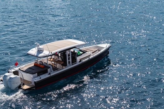 The large luxury boat on the background of blue water, port of Hercules in Monaco, sunny glare of the sun on the water, powerful boat, glossy surfaces shine in sunny weather. High quality photo