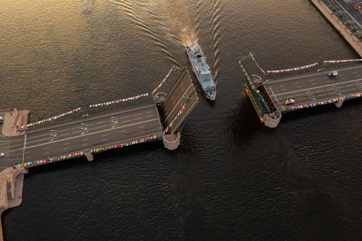 Aerial landscape of warship pass under a raised Palace drawbridge, top view, black color of water, the Neva River before the holiday of the Russian Navy at early morning. High quality 4k footage