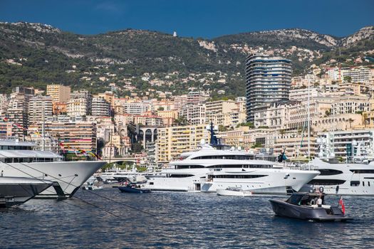 A lot of huge yachts are in port of Monaco at sunny day, megayachts are moored in marina, is a yacht show, Monte Carlo, real estate housing is on background, glossy board of the motor boat. High quality photo