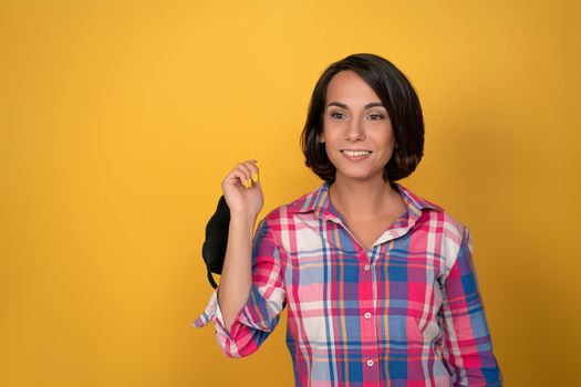 Happy smiling woman holding protective face mask in hand isolated on yellow background. Quarantine ending concept. Copy space at left side.