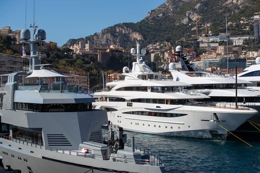 A lot of huge yachts are in port of Monaco at sunny day, megayachts are moored in marina, is a yacht show, Monte Carlo, real estate housing is on background, glossy board of the motor boat. High quality photo