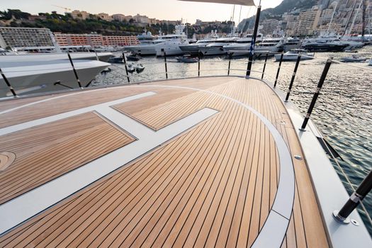 The front deck of huge yacht in port of Monaco at sunset, the place for landing of helicopter, a lot of motorboats are on background, the chrome plated handrail, megayacht is moored in marina, dusk. High quality photo