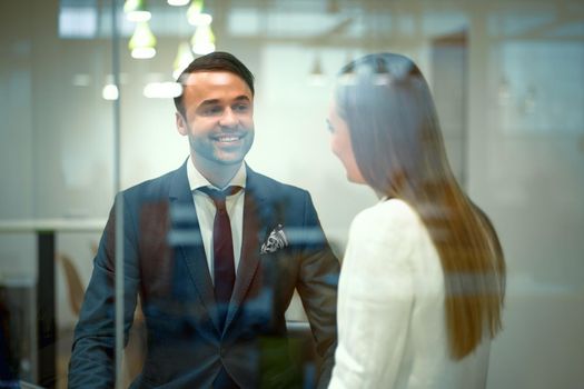 Diverse millennials in formal outfit business partners talking after meeting sitting in a modern bright working place. Handsome young businessman and a woman cooperating working in the office.