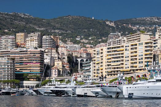 A lot of huge yachts are in port of Monaco at sunny day, megayachts are moored in marina, is a yacht show, Monte Carlo, real estate housing is on background, glossy board of the motor boat. High quality photo