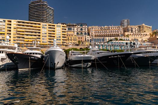 A lot of huge yachts are in port of Monaco at sunny day, megayachts are moored in marina, is a yacht show, Monte Carlo, real estate housing is on background, glossy board of the motor boat. High quality photo