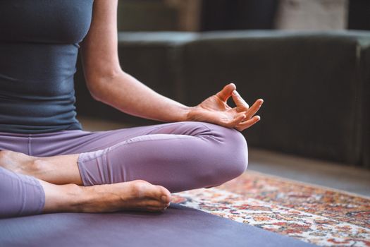 Woman Sitting in Lotus Pose and Meditating with Open Hands. Yoga Female Practicing Yoga Meditation Exercise on the Mat in her Living Room at Home. Close-up. High quality photo