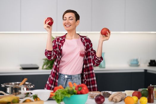 Happy housewife wearing plaid shirt with a short hairstyle with fresh apples in hands cooking apple pie standing at the kitchen. Healthy food at home. Healthy food leaving concept.