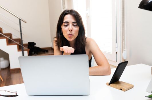 Young caucasian woman blowing a kiss goodbye during video call with a friend at home. Technology and communication concept.