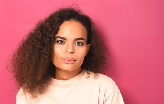 Whistling lips folded happy beautiful young African American woman looking positively at camera wearing peachy t-shirt isolated on pink background. Beauty concept.