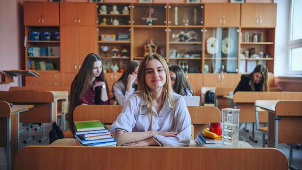 Schoolgirl poses with textbooks at her desk in her class