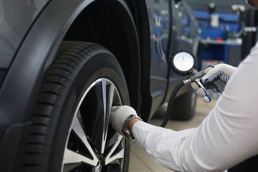 Close-up of automechanic pumping up tires with special instrument at work. Qualified worker fix machine on station. Car maintenance, repair service concept