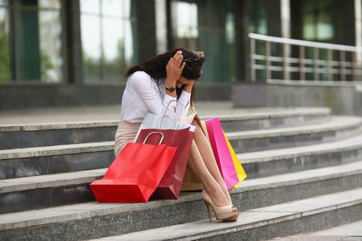Portrait of upset woman sit on staircase, close face with hands, spent all money on clothes. Depressed person after silly shopping. Broken, beggar concept
