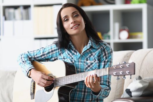 Portrait of pretty brunette woman playing on guitar in living room, female spend free time to learn new hobby on musical instrument. Music, hobby concept