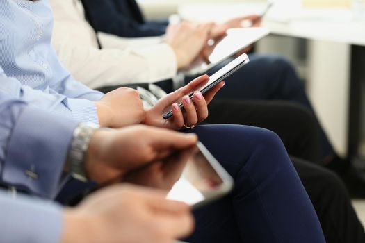 Close-up of people using mobile phones on meeting, modern gadgets in work. Team making notes on smartphones, listen to speech. Business meeting concept