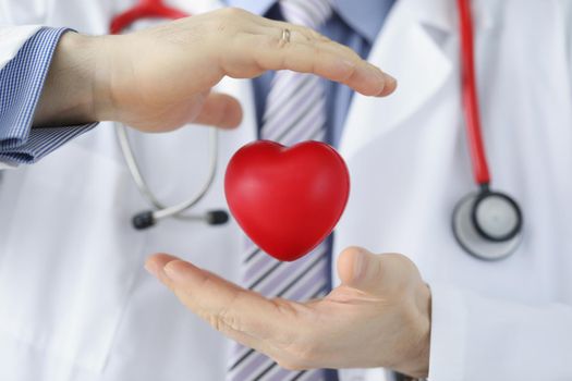 Close-up of medical worker protect plastic red heart, doctor cover heart model with hands. Save life, donation and charity. Cardiology, healthcare concept