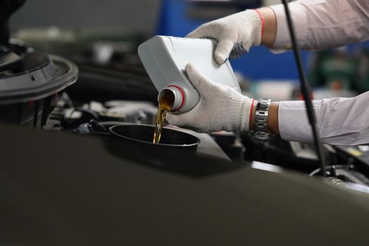 Close-up of man in gloves refueling and pour new fresh oil into engine motor car. Handyman from maintenance service fix auto. Maintenance, pitstop concept