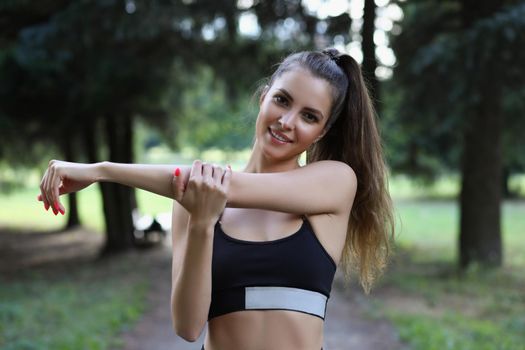 Portrait of young woman stretching arms before morning workout on fresh air. Active sportswoman smiling on camera. Active lifestyle, hobby, sport concept