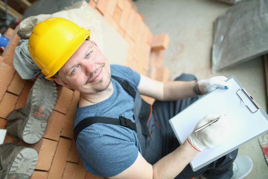 Top view of busy foreman worker make plan for further construction works on object. Male smiling in protective uniform. Construction site, building concept