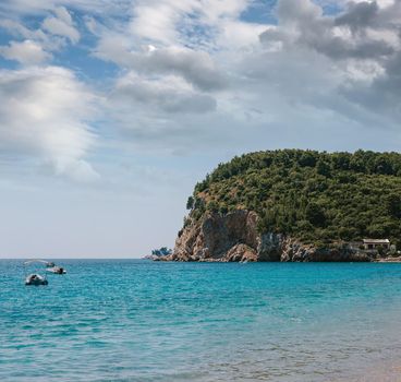 Picturesque view on rocks on a sunny day from the sea. Budva riviera, Montenegro. Aerial view of Sveti Nikola, Budva island, Montenegro. Hawaii beach, umbrellas and bathers and crystal clear waters. Jagged coasts with sheer cliffs overlooking the transparent sea. Wild nature. The rocky shore of Island St.Nikola near Budva, Montenegro. Picturesque summer view of Adriatic sea coast in Budva Riviera.