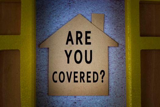 Are you covered text on house paper model with window frame background. Home insurance concept. Flat lay. Directly above.