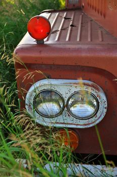 Close up of Headlight of an Abandoned Vintage and Rusty Truck in the long grass of a Farm Field on a Sunny Day. High quality photo