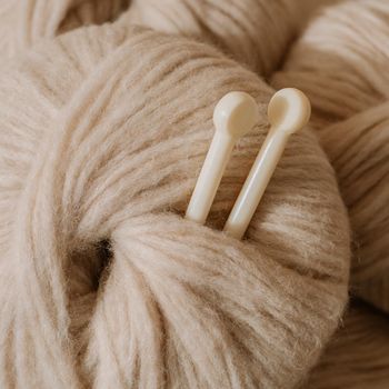 Aesthetic image of pastel beige light, airy yarn skein.Close up view of medium thick blow yarn made of baby alpaca and merino wool. Knitting needles stuck in skein of yarn.Square crop for social media