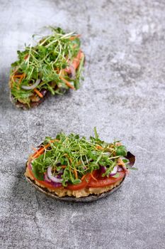 Sandwich toasted rustic bread with chickpea hummus, tomato slices, mix of lettuce and microgreens. Vegetarian breakfast.